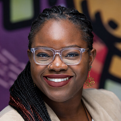 Headshot of Eniola Abioye. She has a medium-dark skin tone, long dark braids, a nose ring, and clear-rimmed glasses.